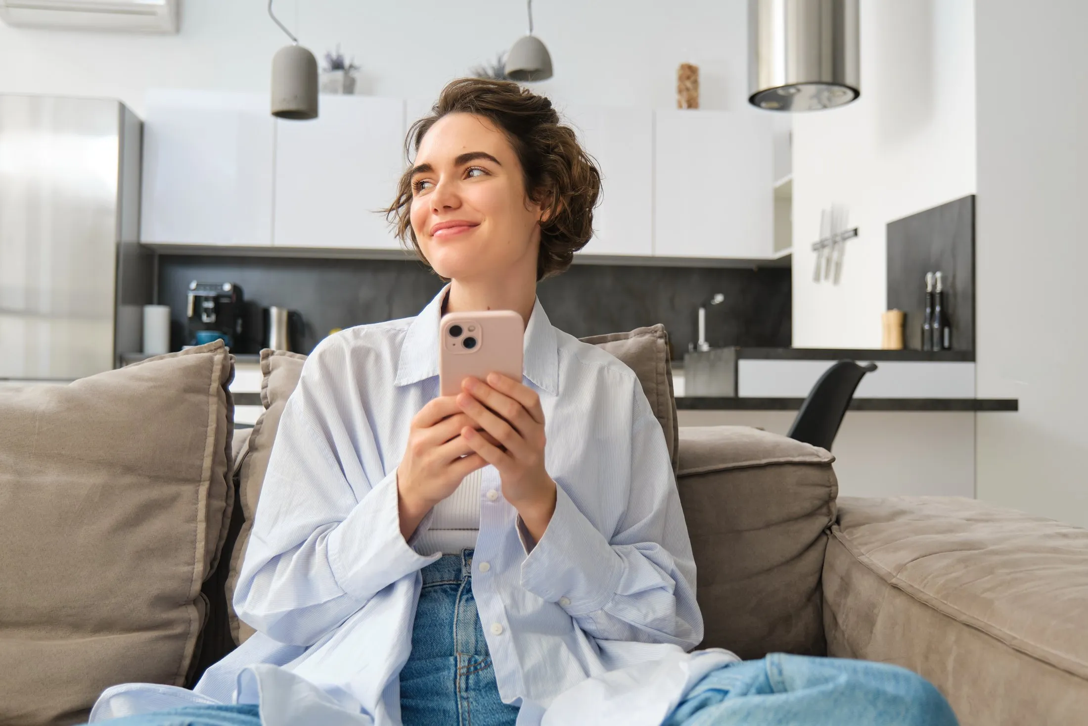 Mulher sorrindo enquanto conversa pelo celular no sofá de casa